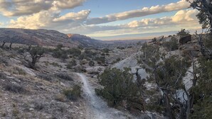 A rugged, rocky terrain with sparse vegetation and a dirt path leading through a mountainous landscape. - Morning Coffee with the quail.  Great views, excellent trails, and work friendly (Grand Junction)