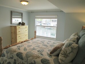 A bedroom with a large bed, a dresser, a window with a view of boats, and a ceiling light. - water at your back door (Cudjoe Key)