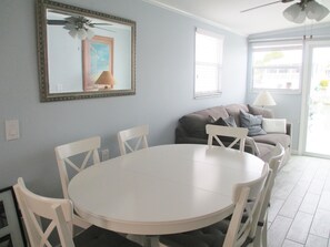 A dining area with a round white table and chairs, a gray sofa with cushions, a ceiling fan, and a large mirror on the wall. - water at your back door (Cudjoe Key)