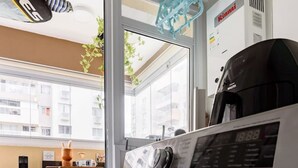 Eine kleine Waschküche mit Waschmaschine und Trockner, eine Küchenzeile und Blick auf die Stadt durch große Fenster.