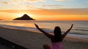 Eine Person mit erhobenen Armen am Strand bei Sonnenuntergang.