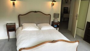 A neatly made bed with a wooden frame and white bedding, two bedside tables with lamps, and a door leading to another room. - Country house nestled in a green setting 15 minutes from Lille (Sainghin-en-Mélantois)