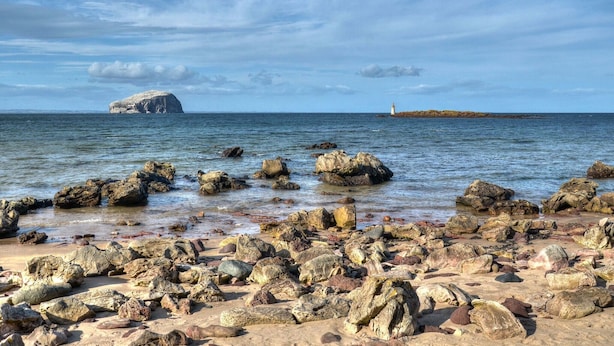 A rocky beach with a lighthouse in the distance.