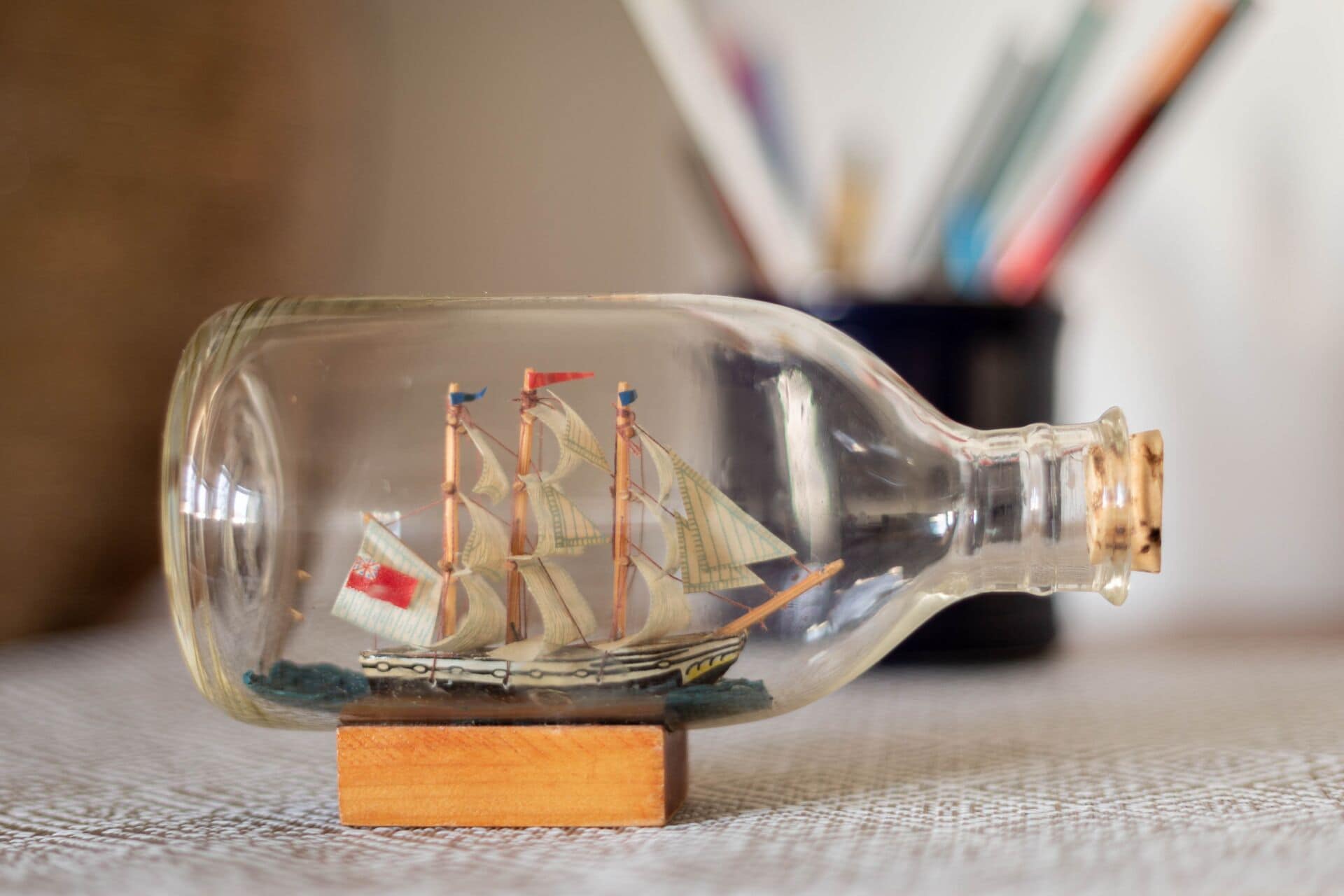 Una botella de vidrio transparente con una maqueta de barco en su interior, sobre una base de madera.