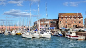 A harbor with multiple boats docked, a stone building with a sloped roof, and a clear blue sky.