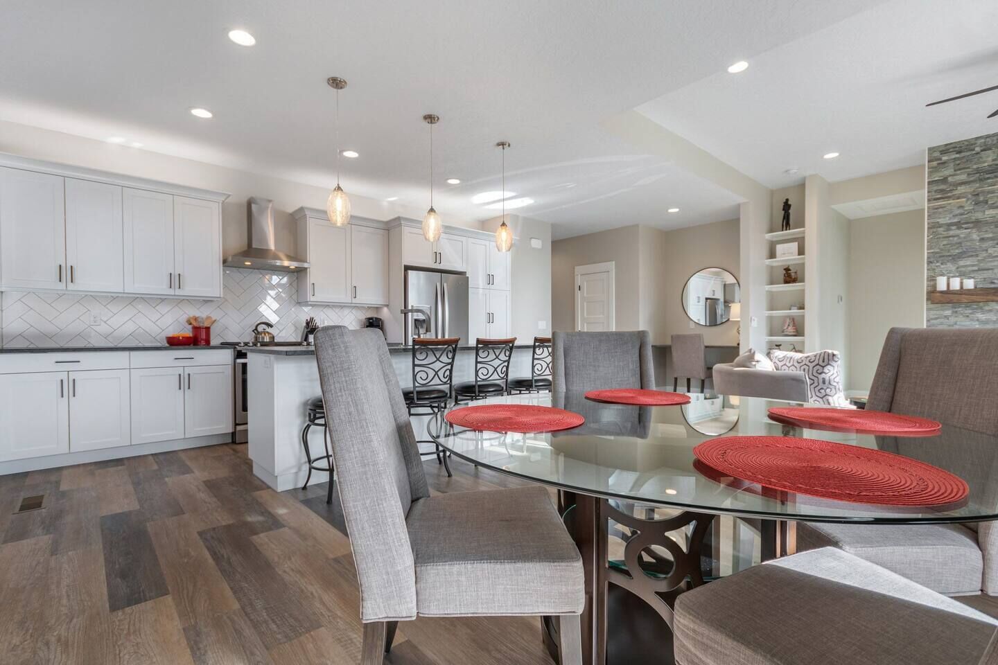 A modern kitchen with white cabinets, a central island, and a dining area with a glass table and grey chairs.