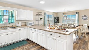 A spacious kitchen with white cabinetry, a central island, and a dining area with a table and chairs. - 🏖 3 Min Walk to the Beach 💦 Ice Machine  🌼 In Quiet Fort Morgan (Gulf Shores)