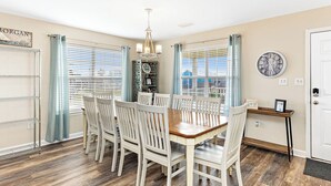 A dining area with a wooden table and white chairs, a chandelier, and a clock on the wall. - 🏖 3 Min Walk to the Beach 💦 Ice Machine  🌼 In Quiet Fort Morgan (Gulf Shores)
