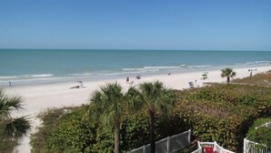 Une plage avec un ciel dégagé, un rivage sablonneux et quelques zones verdoyantes.