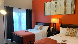 A hotel room with two beds, a large window with curtains, a floor lamp, and a painting on the wall. - A Cozy Bellevue Condo at CrossRoad Mall (Bellevue)