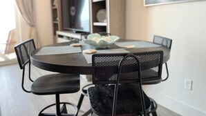 A dining area with a round table and four chairs, a bowl of fruit, and a television in the background.
