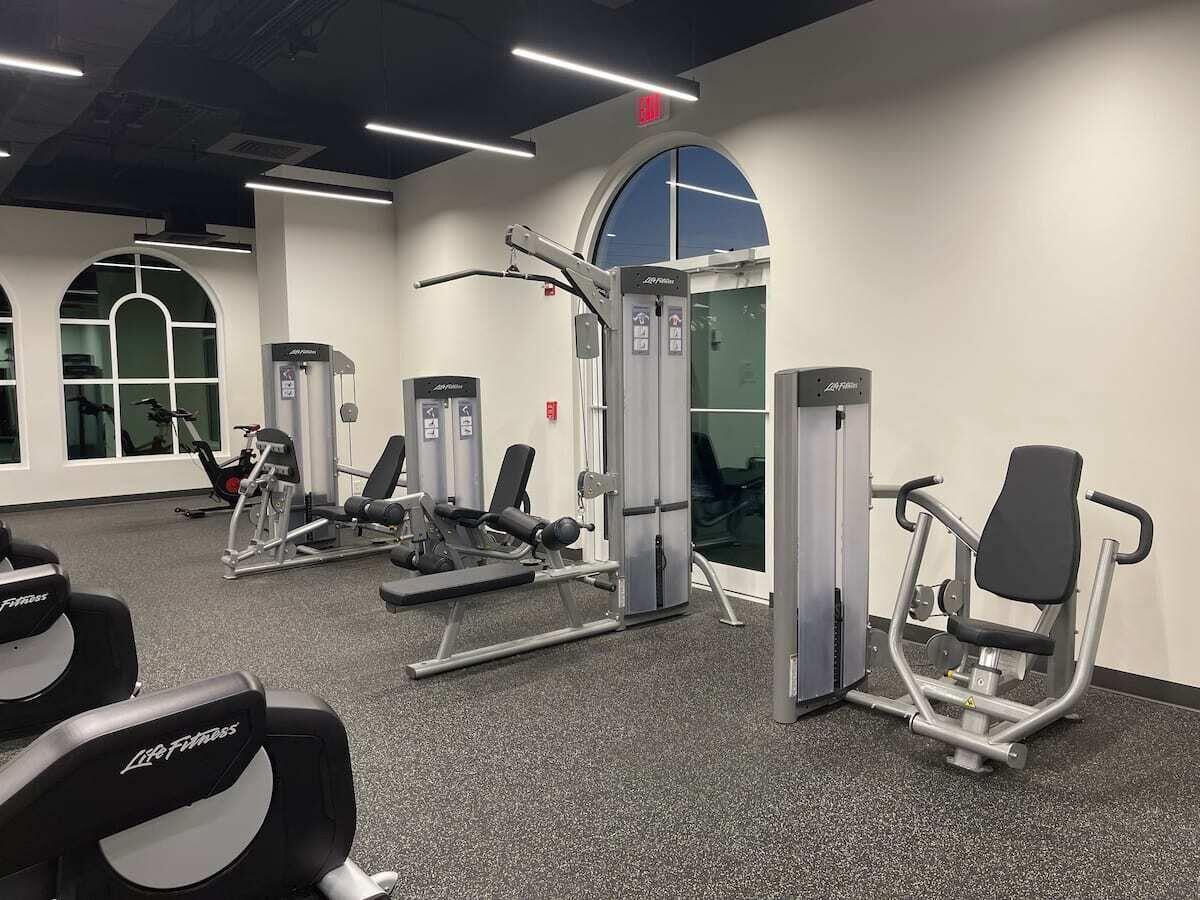 A gym with various exercise machines, a large window, and a door.