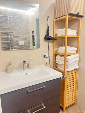 A bathroom with a white sink, a mirror, a towel rack, and a wooden shelf with folded towels. - Monem's House-door (Milano)