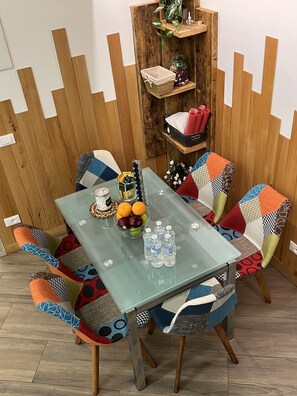 A dining area with a glass table, colorful chairs, and a wooden wall with shelves. - Monem's House-door (Milano)