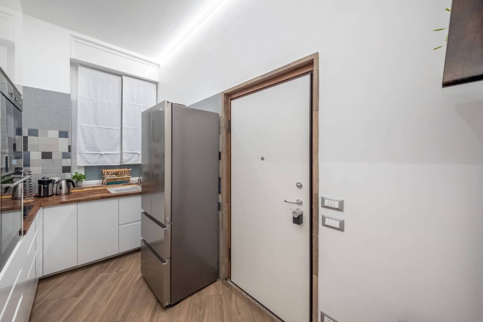 Una cocina moderna con un refrigerador de acero inoxidable, gabinetes blancos y una encimera de madera.