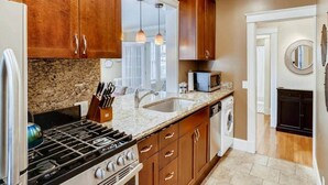 A kitchen with wooden cabinets, a granite countertop, a stove, a sink, and a microwave. - Historic 2BR Apt in ❤️ of DT Seattle Free Parking+ (Seattle)