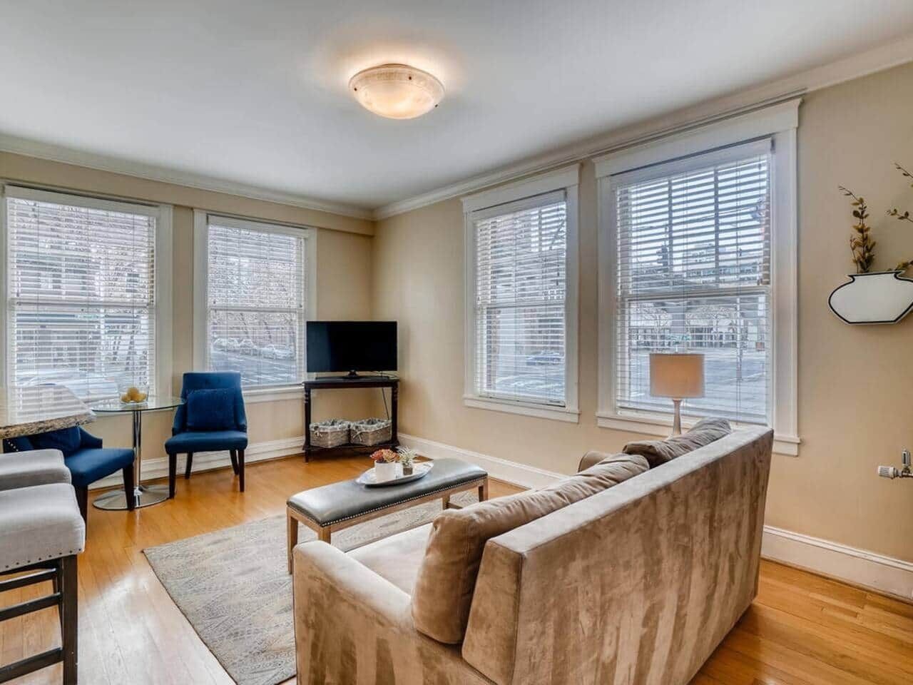 A living room with a sofa, armchair, TV stand, and large windows.