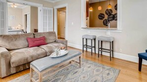 A living room with a beige sofa, a small table with a tray, and two bar stools. - Historic 2BR Apt in ❤️ of DT Seattle Free Parking+ (Seattle)
