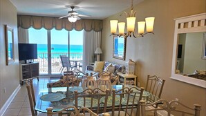 A spacious living room with a large glass table, comfortable seating, a ceiling fan, and a view of the ocean. - Exceptional Luxury Gulf-Front Condo at Summer Place! (Fort Walton Beach)