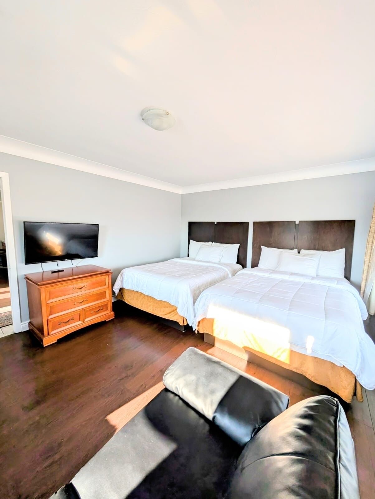 Una habitación de hotel con dos camas, un aparador de madera, una televisión y un ventanal grande.