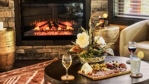 Una habitación acogedora con chimenea, una mesa redonda con tabla de quesos, copas de vino y un centro de mesa decorativo.