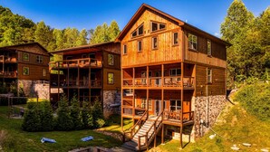 Una cabaña de madera de varios pisos con balcones, un cimiento de piedra y una pequeña zona con fogata.