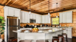 Una cocina moderna con armarios blancos, electrodomésticos de acero inoxidable y una isla central con taburetes.