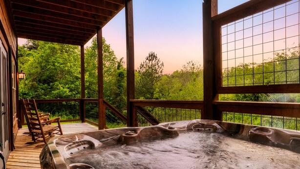 Un jacuzzi en una terraza de madera con vistas a árboles y un cielo despejado.