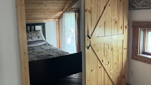 A bedroom with a wooden ceiling, a bed, and a large sliding barn door. - Echo Lake Lakefront Cabin in picturesque Qu’Appelle Valley,  (Fort san)