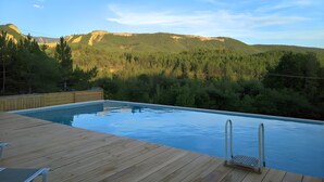 A swimming pool with a wooden deck, surrounded by forested hills.