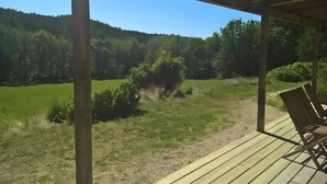 A wooden deck with a bench, overlooking a grassy field and forested hills.