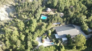 An aerial view of a property with a large building, a swimming pool, and a circular structure surrounded by trees.