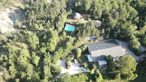 Vogelperspektive auf ein Anwesen mit einem großen Gebäude, einem Swimmingpool und einer von Bäumen umgebenen, runden Struktur.