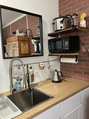A kitchen with a sink, a mirror, a stove, a microwave, and shelves with kitchenware.