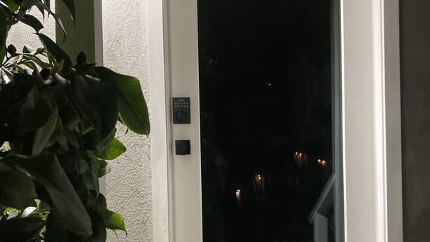 Valkoinen ovi, jossa on lasiruutu, pieni elektroninen näppäimistö ja geometrisesti kuvioitu ovimatto.