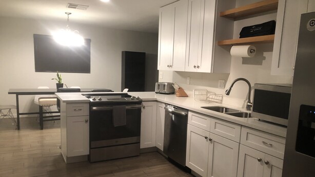 Una cocina moderna con armarios blancos, electrodomésticos de acero inoxidable, suelo de madera y un comedor con mesa y sillas.