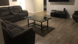 Una sala de estar moderna con televisor de pantalla plana, sofás de cuero, una mesa de centro de vidrio y piso de madera.