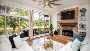 A spacious living room with a large window, a fireplace, and a ceiling fan. - ***THE C5 RIVER HOUSE MINUTES FROM MAGNOLIA AND BAYLOR RIVER *** (China Spring)