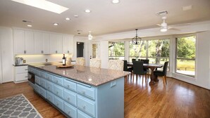A spacious kitchen with a large island, light blue cabinetry, and a dining area with a table and chairs. - ***THE C5 RIVER HOUSE MINUTES FROM MAGNOLIA AND BAYLOR RIVER *** (China Spring)