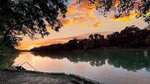 A serene lakeside view with a sunset, calm water, and a stone border along the shore. - ***THE C5 RIVER HOUSE MINUTES FROM MAGNOLIA AND BAYLOR RIVER *** (China Spring)