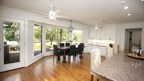 A modern kitchen with white cabinets, a granite countertop, and a dining area with a wooden table and chairs. - ***THE C5 RIVER HOUSE MINUTES FROM MAGNOLIA AND BAYLOR RIVER *** (China Spring)