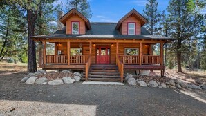 A log cabin with a front porch, a red door, and a stone chimney. - Log cabin with game room by skiing & lake (McCall)
