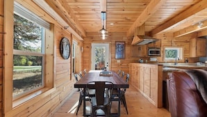 A wooden cabin interior with a dining area, kitchen, and large windows. - Log cabin with game room by skiing & lake (McCall)