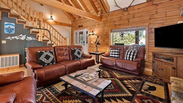 A log cabin interior with a staircase, leather sofas, a coffee table, and a television. - Log cabin with game room by skiing & lake (McCall)