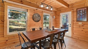 A wooden cabin with a dining table and chairs, large windows, and a ceiling light fixture. - Log cabin with game room by skiing & lake (McCall)