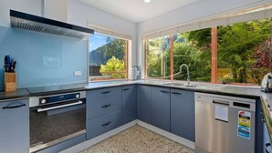 Una cocina moderna con lavavajillas, estufa y lavabo. Cuenta con ventanas amplias que ofrecen vistas a zonas verdes y una montaña.