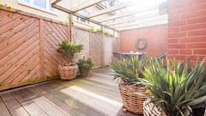 Una terraza de madera con cercado de madera, plantas en macetas y una parrilla.