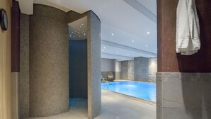 Una piscina interior con suelo y paredes de azulejos, techo con iluminación empotrada y una silla cerca de la piscina.