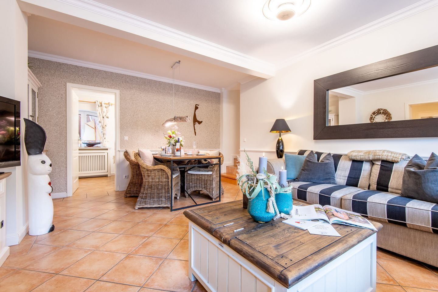 Uma sala de estar com sofá, mesa de centro e área de jantar com cadeiras de vime.