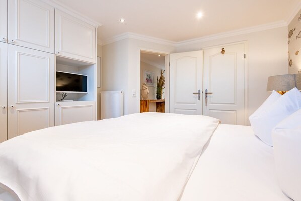 A hotel room with a large bed, white walls, and a wardrobe with a television.